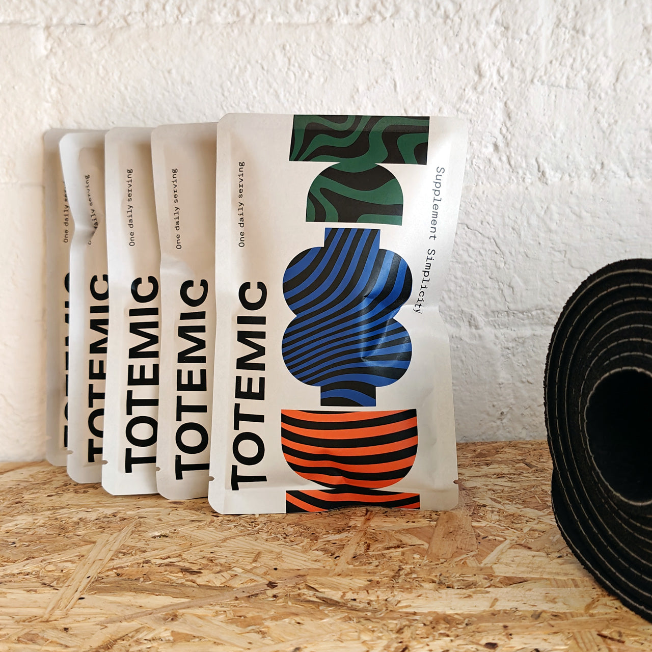 Packages of TOTEMIC sachets on a wooden surface with a white textured wall in the background. 