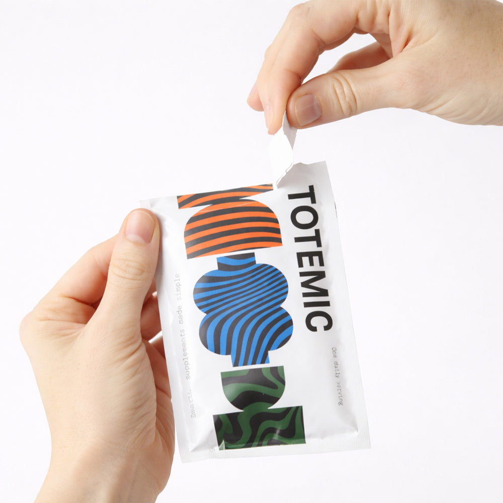 hands tearing open a TOTEMIC supplement sachet against a white background